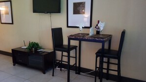Una habitación pequeña y limpia con escritorio, dos sillas, televisor y cuadros en la pared.
