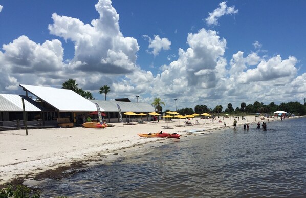 A beach with kayaks, umbrellas, and a building with a white roof.