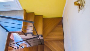 A wooden staircase with a glass railing leading to a room with a yellow wall and a decorative object on the wall. - Sperlinga kept - Il Campanile (Santa Flavia)