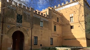 A historic building with a large arched entrance, multiple windows, and a courtyard with plants. - Sperlinga kept - Il Campanile (Santa Flavia)