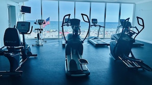 Et fitnessrum med træningsmaskiner og udsigt til stranden.