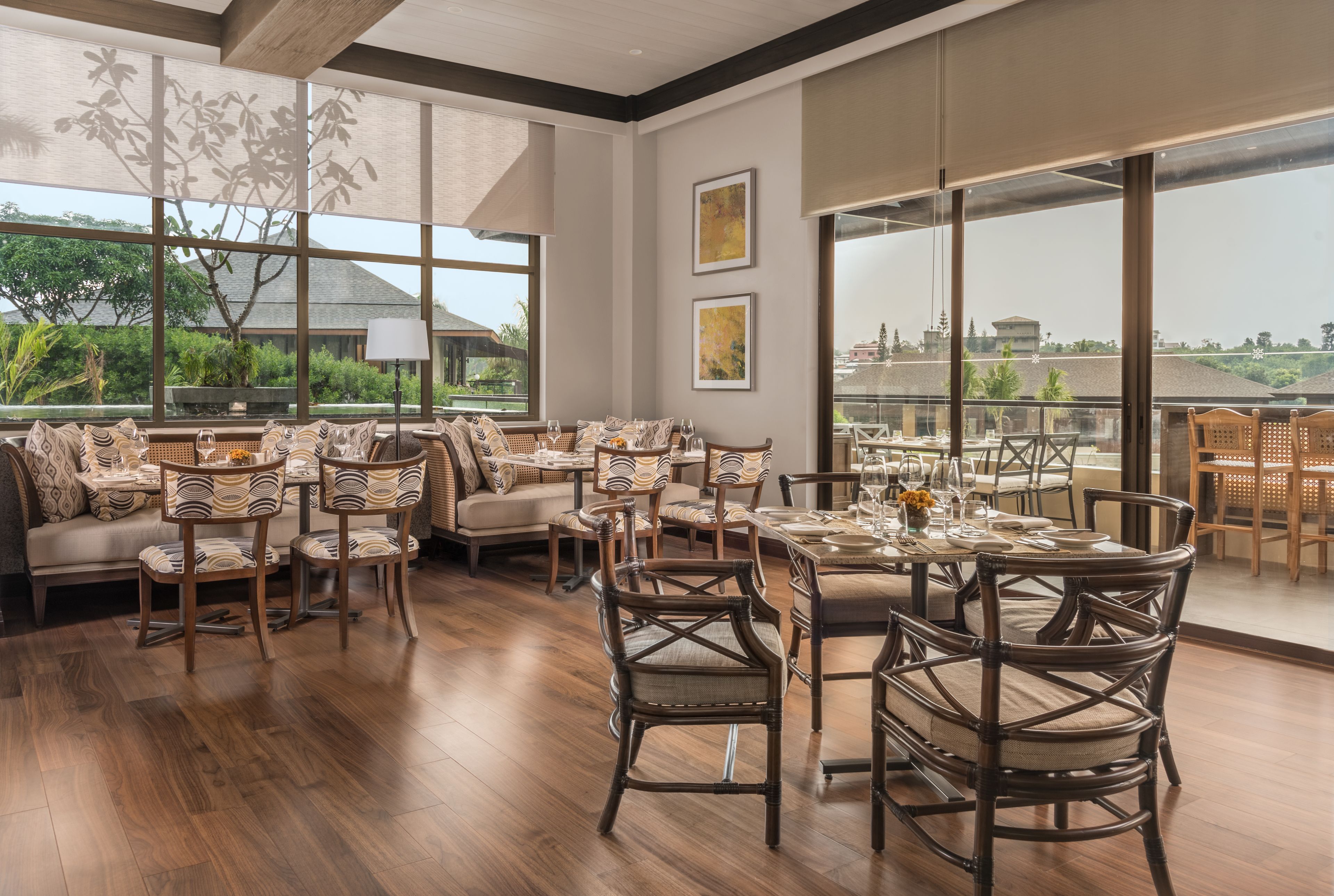 A spacious dining area with wooden flooring, wicker furniture, and large windows offering a view of the outdoors.