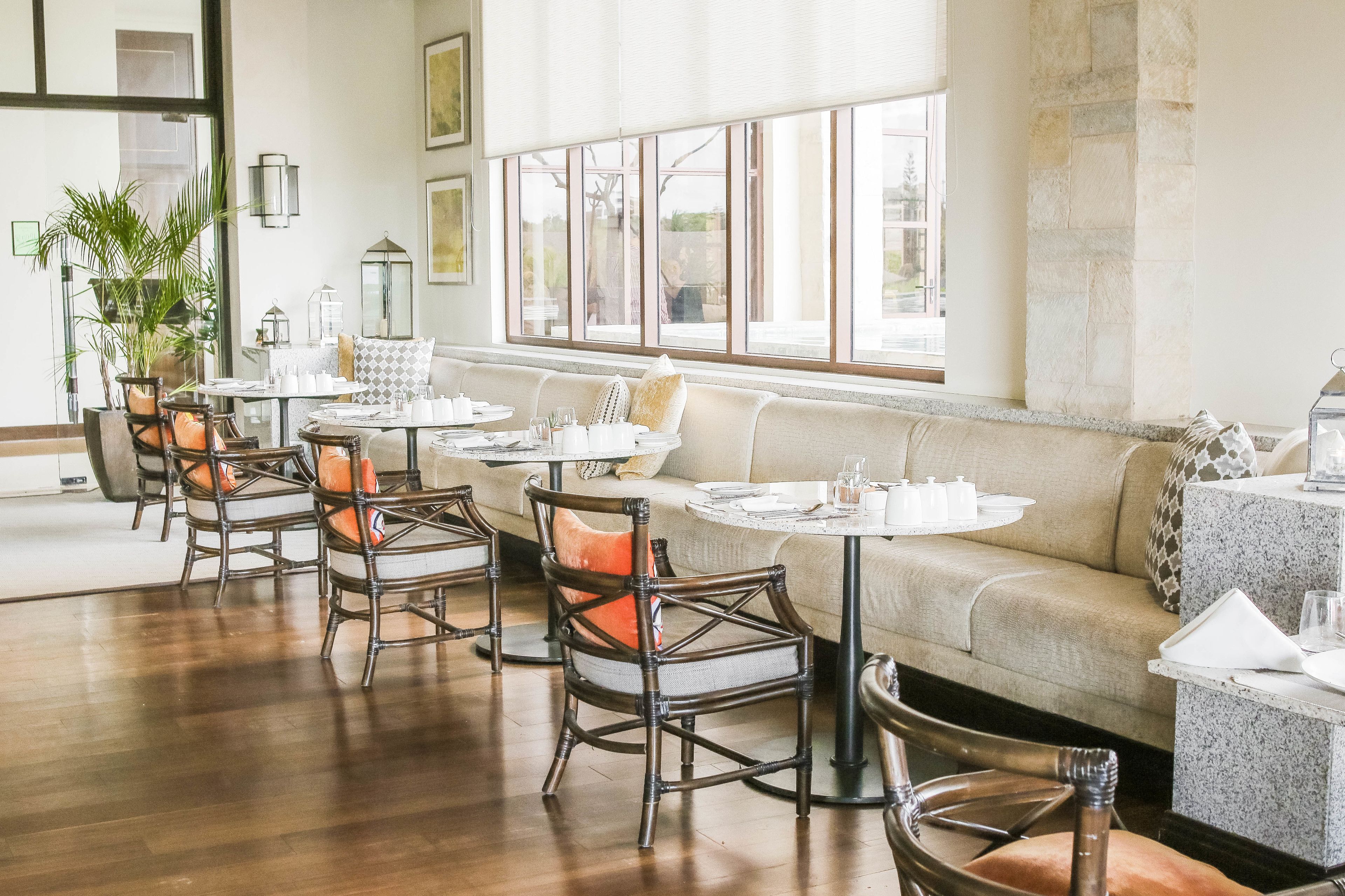 Un comedor con mesas redondas, sillas de mimbre y un sofá beige.