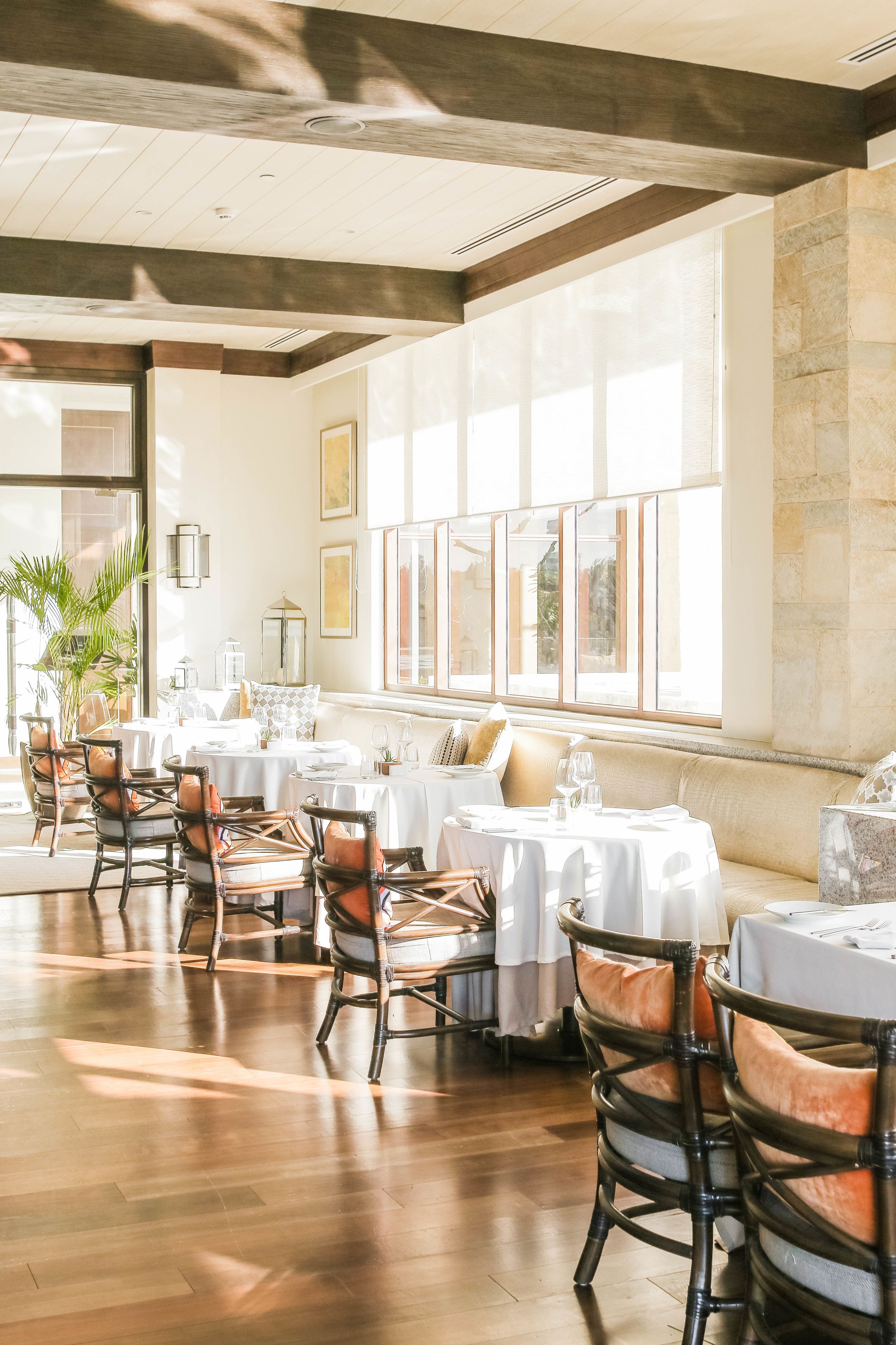 A restaurant with round tables, cushioned chairs, and large windows allowing natural light.