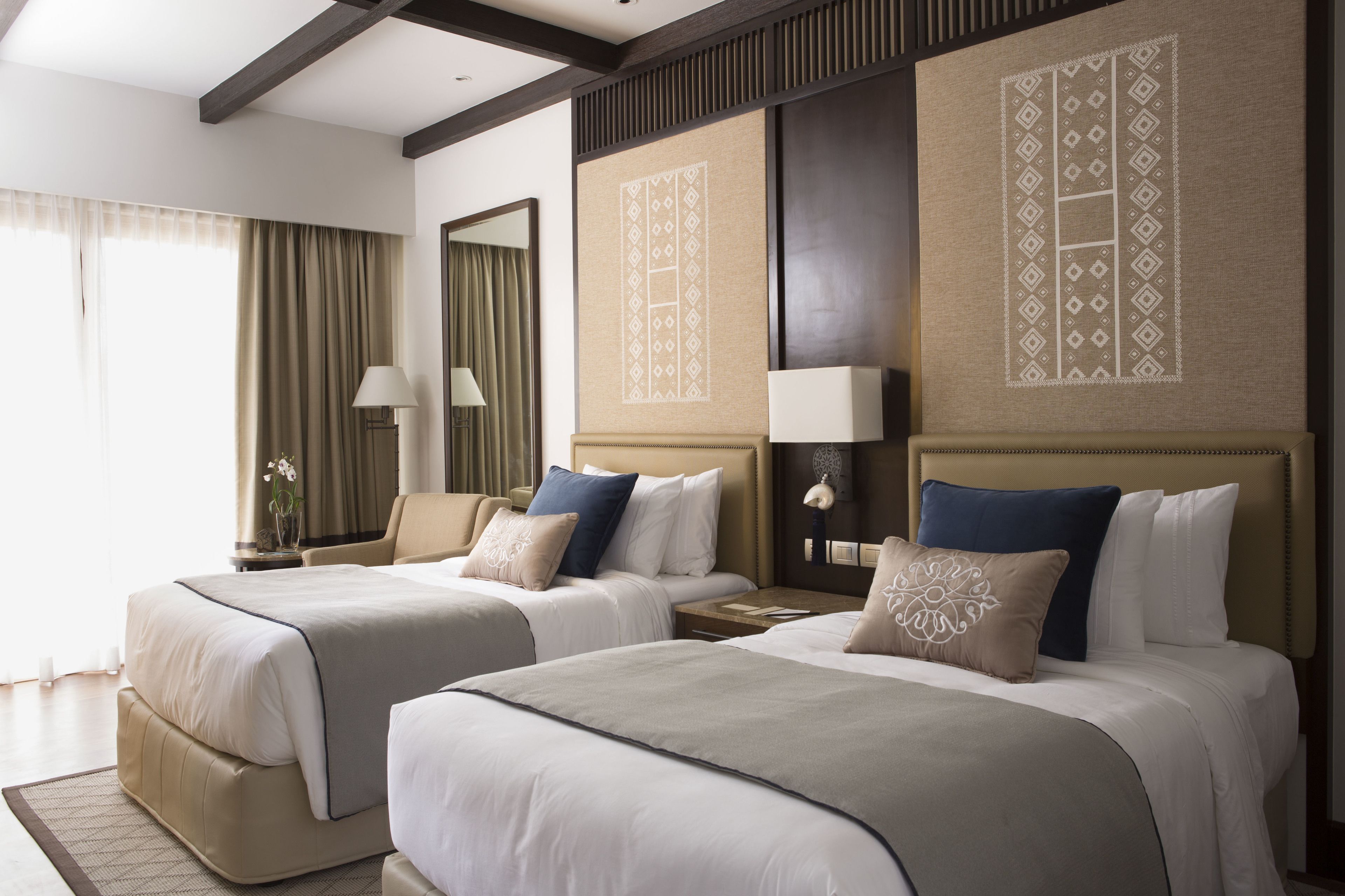 Quarto de hotel com duas camas, um espelho grande e um painel decorativo na parede.