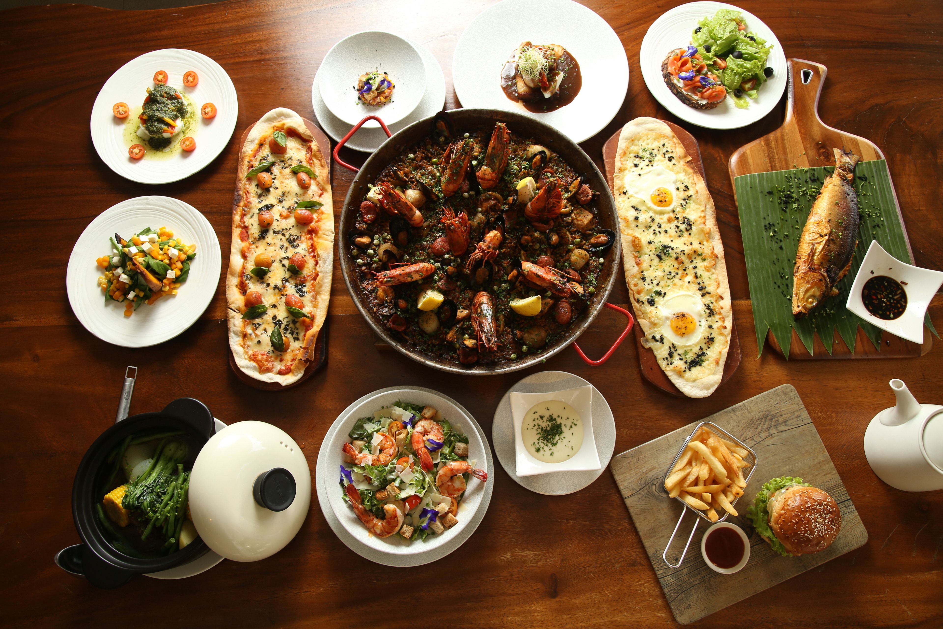 Une variété de plats, notamment des fruits de mer, des salades et du pain, présentés sur une table en bois.