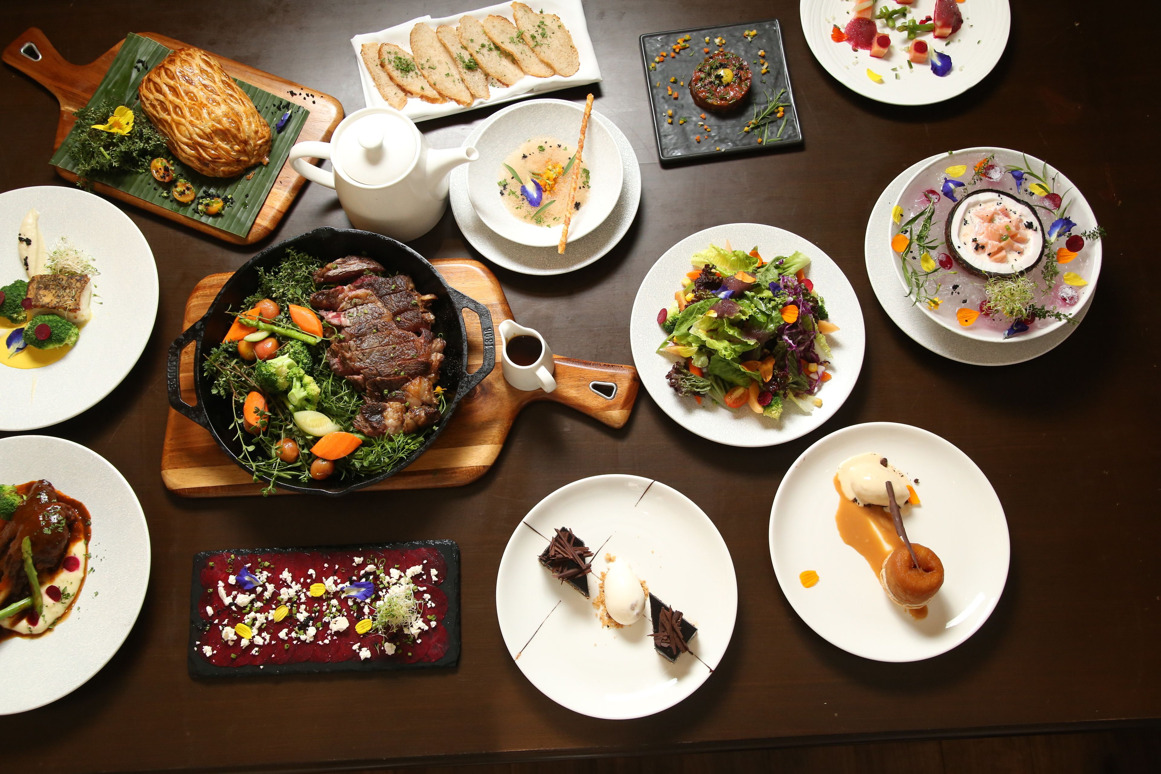 A variety of dishes on a table, including a steak, salad, and dessert.