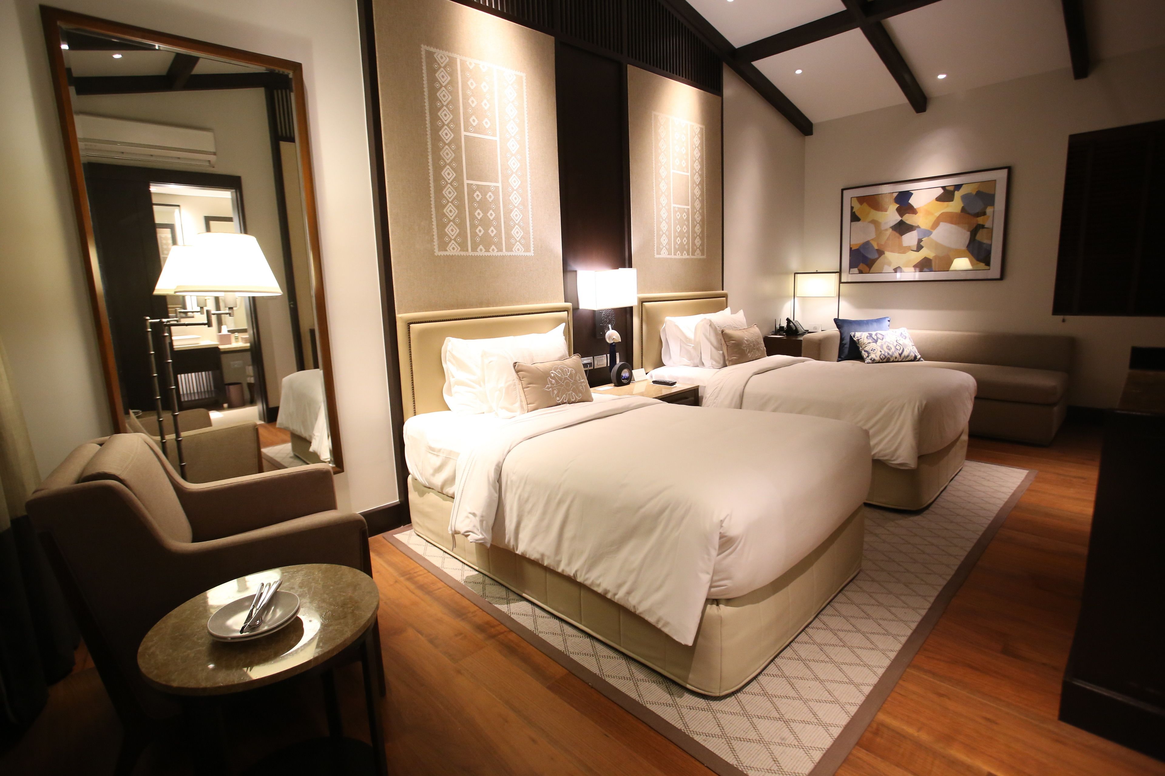 A hotel room with two beds, a sitting area with a table, a mirror, and artwork on the walls.