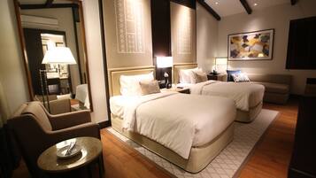 A hotel room with two beds, a sitting area with a table, a mirror, and artwork on the walls.