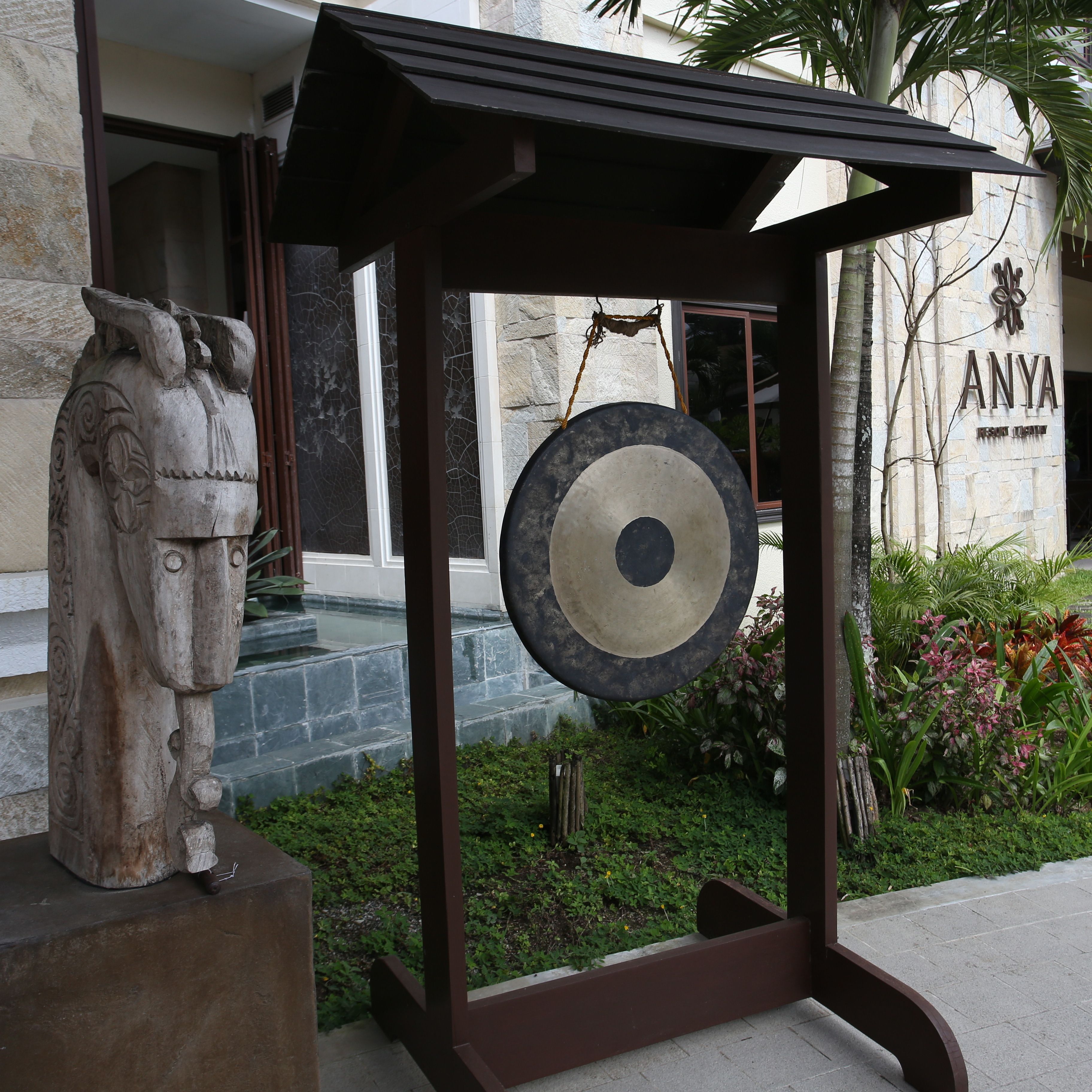Una estatua de piedra, una campana circular y un edificio con el nombre 'ANYA' en la fachada.
