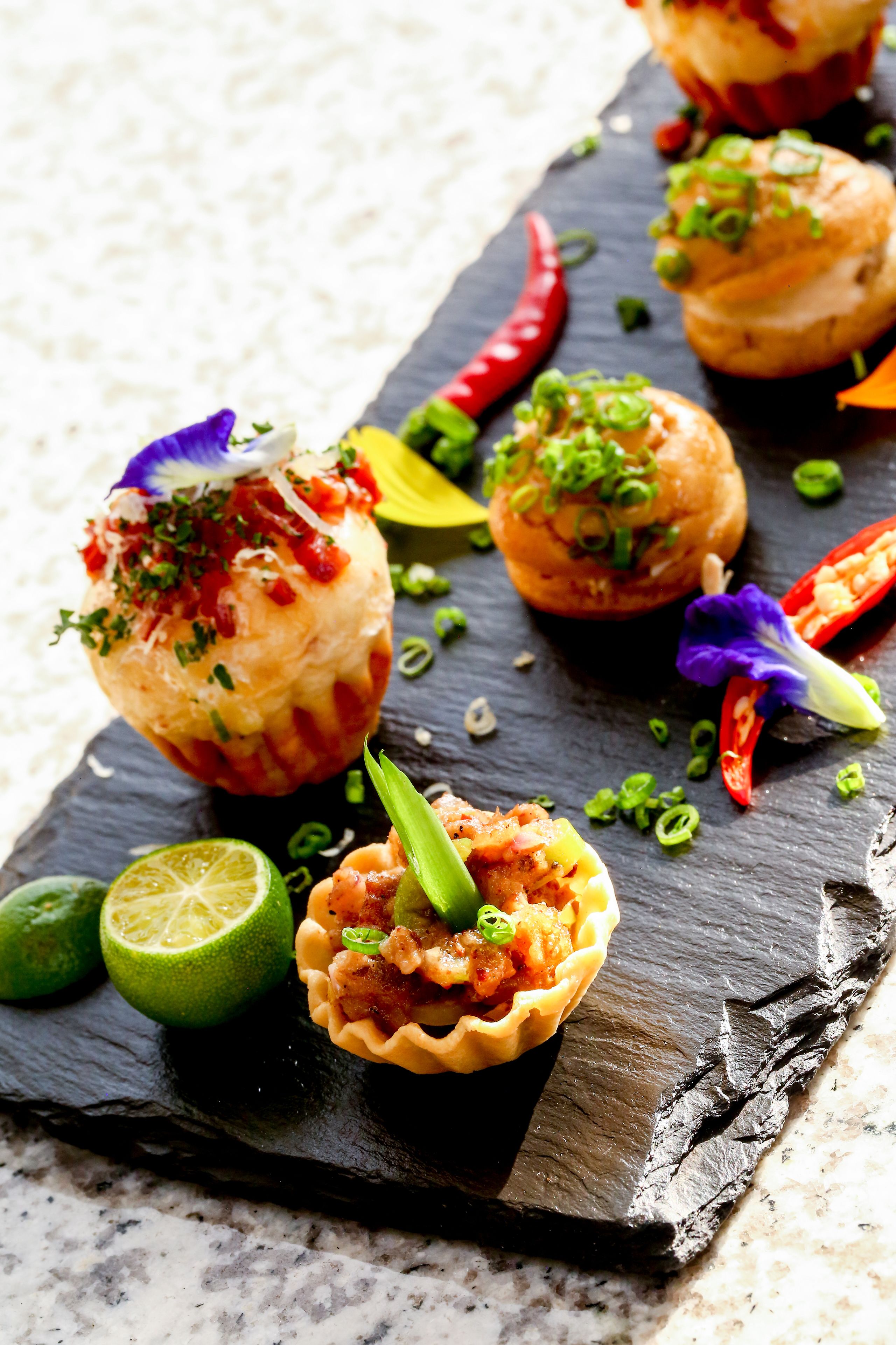 A variety of appetizers on a slate serving board, including shrimp and other seafood items, garnished with herbs and edible flowers.