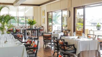 A restaurant with multiple tables and chairs, large windows, and potted plants.