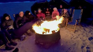 Un grupo de personas sentadas alrededor de una fogata en la playa, de noche.