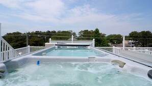 Un jacuzzi con muelle blanco y barandillas, rodeado de árboles y un cielo despejado.