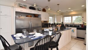 Una cocina moderna con armarios blancos, una isla central con asientos, electrodomésticos de acero inoxidable e iluminación colgante.