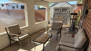 A covered patio area with outdoor furniture, a grill, and a shed in the background. - Beautifully Charming Redbrick Home (Phoenix)