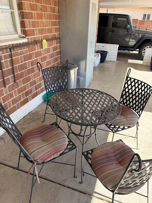 Eine Terrasse mit einem runden Metalltisch, vier Stühlen, einem Mülleimer und einer Ziegelwand.