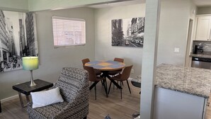 A modern living room with a dining area, a patterned armchair, a table with a placemat, and a kitchen visible through an open doorway. - Beautifully Charming Redbrick Home (Phoenix)