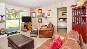 A living room with a leather sofa, a television, a cabinet with decorative items, and a view of a garden through a sliding door. - 2 BR Condo with 2 Fishing Badges! 24 Mi. to Aspen (Carbondale)