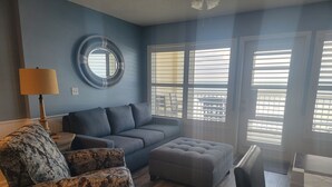Ein Wohnzimmer mit blauer Wand, einem runden Spiegel, einem grauen Sofa, einem gemusterten Sessel und einem grauen Ottomanen.