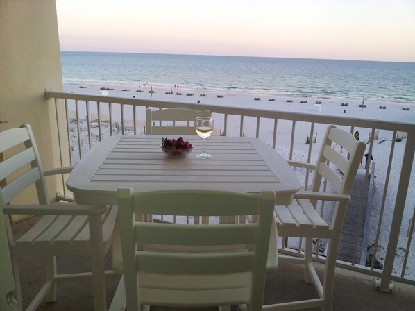 A balcony with a table, chairs, and a bowl of fruit.