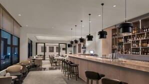 A modern bar area with a long counter, multiple bar stools, and a well-stocked liquor shelf.