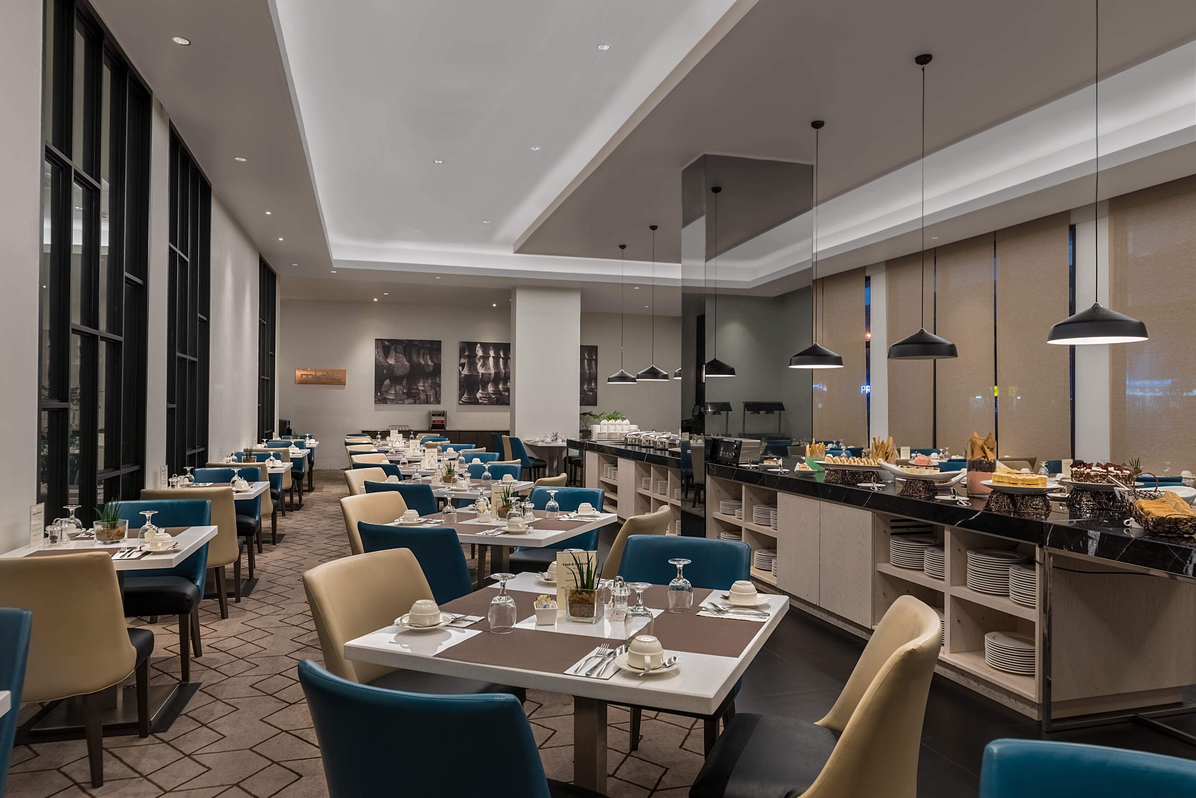 A modern dining area with tables set for service, a buffet counter, and a view of the cityscape through large windows.