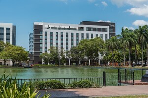 A modern hotel with a large water feature in front, surrounded by greenery and palm trees.