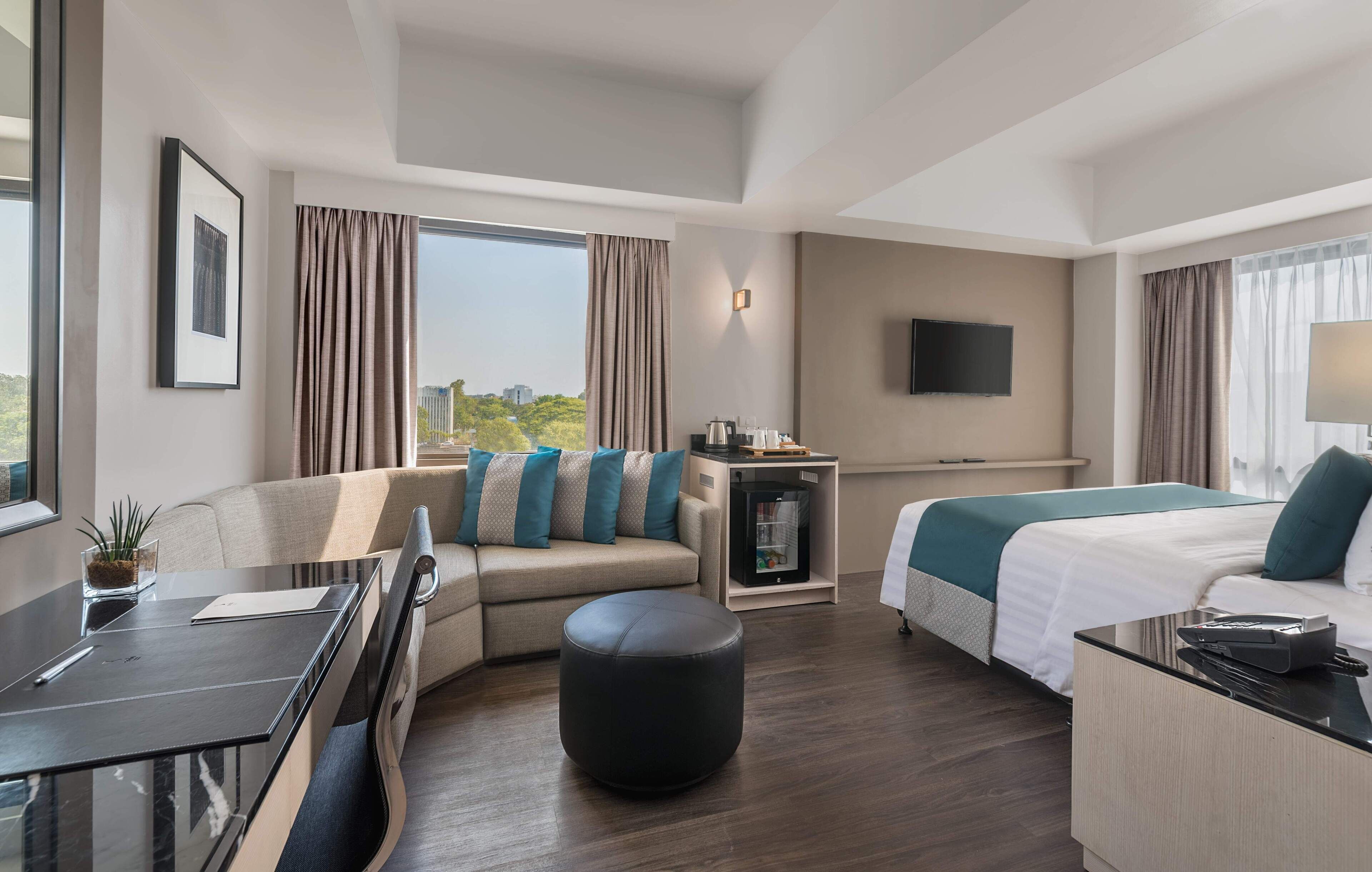 A modern hotel room with a sofa, a bed, a desk, and a television.