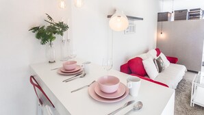 A modern kitchen with a white countertop, pink and white dishes, and a red sofa in the background. - Pinnacle PJ Penguin Homes (Petaling Jaya)