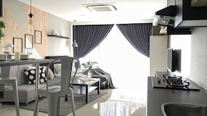 A modern living room with a sofa, coffee table, and dining area. There is a kitchen with a stove and sink. - Pinnacle PJ Penguin Homes (Petaling Jaya)