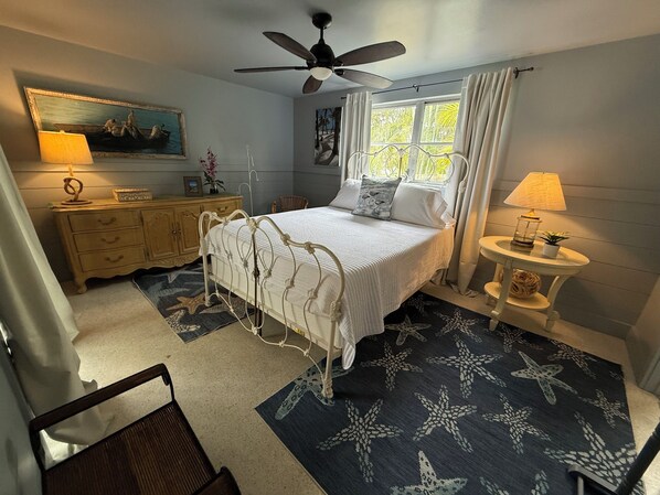 A bedroom with a bed, a ceiling fan, a window with curtains, a nightstand, a dresser, and a chair.