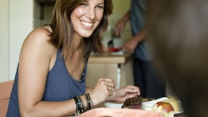 A dining area with a table set for two, a person preparing food in the background, and a basket of food items on the table. - Apartment for 2 - 3 people (Wängle)