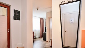 A hallway with a wooden floor, a door with a light switch, a small table, and a chair. - Apartment for 2 - 3 people (Wängle)