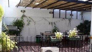 A covered outdoor area with a table and chairs, potted plants, and an air conditioning unit. - Hostel Lagares (Mendoza)