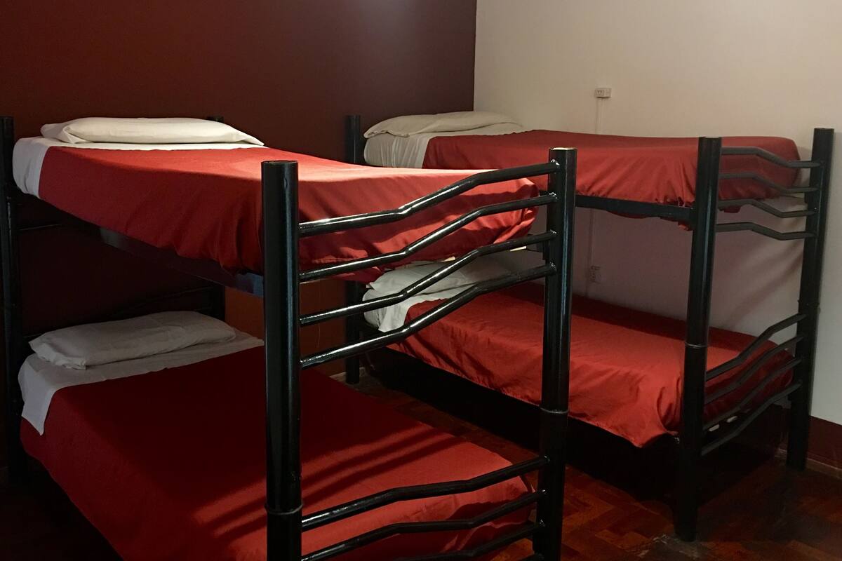 Habitación con literas de tres plazas, cada una con colchón rojo y almohadas blancas.