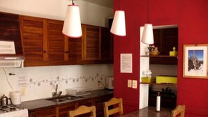A kitchen with wooden cabinets, a granite countertop, and a red wall. There are two pendant lights, a stove, and a sink. - Hostel Lagares (Mendoza)
