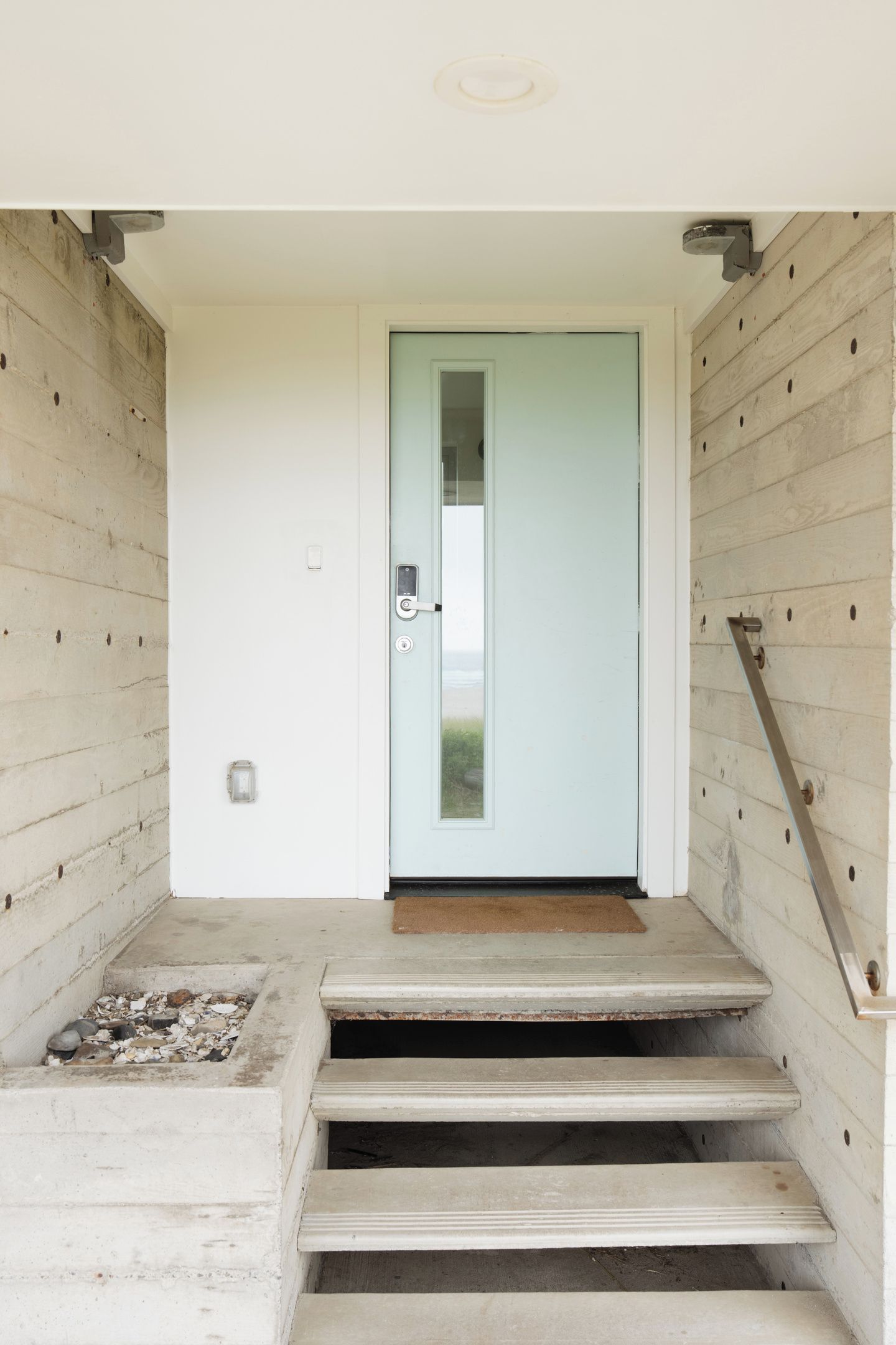 A staircase leading to a door with a light blue frame, a doormat, and a light switch on the wall.