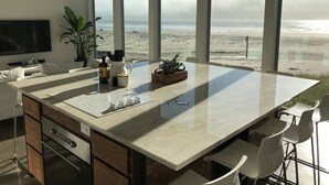 Cozinha moderna com uma ilha grande, amplas janelas com vista para a praia e uma área de jantar com banquetas.