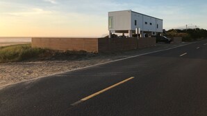 Um edifício moderno com telhado plano, situado perto de uma praia sob um céu claro.
