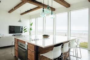 Eine moderne Küche mit einer großen Kochinsel, Barhocker und Blick auf den Strand.