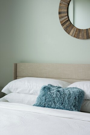 A bed with white bedding and a single blue textured pillow.