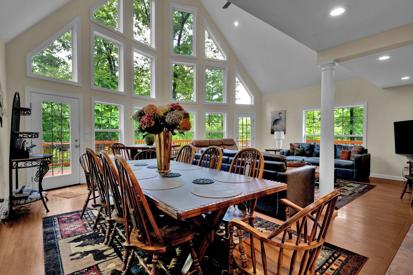 Un vaste espace dédié à la salle à manger, avec une grande table et des chaises en bois, le tout entouré de grandes fenêtres offrant une vue sur la verdure.