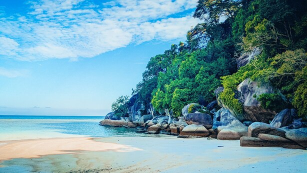 A beach with clear turquoise water, a sandy shore, and large rocks.