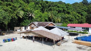 A beachside village with thatched-roof huts, a white building with a red roof, and solar panels.