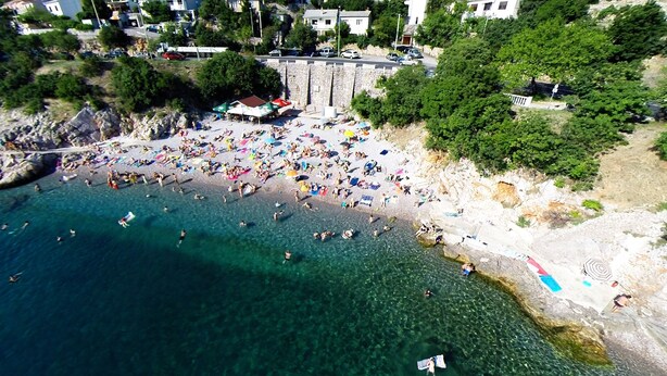 Vista aerea di una spiaggia con acqua cristallina, persone che nuotano e ombrelloni.