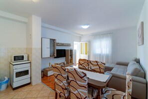Een moderne woonkamer met een bank, eettafel en stoelen. Er is een keuken met een magnetron en oven.