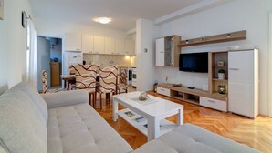 Un soggiorno moderno con divano, tavolino e mobile TV. È presente una zona cucina con pensili e un tavolo da pranzo.