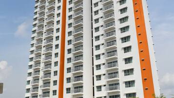 Un edificio alto con varios balcones, una franja naranja en el centro y un estacionamiento con flechas indicativas.