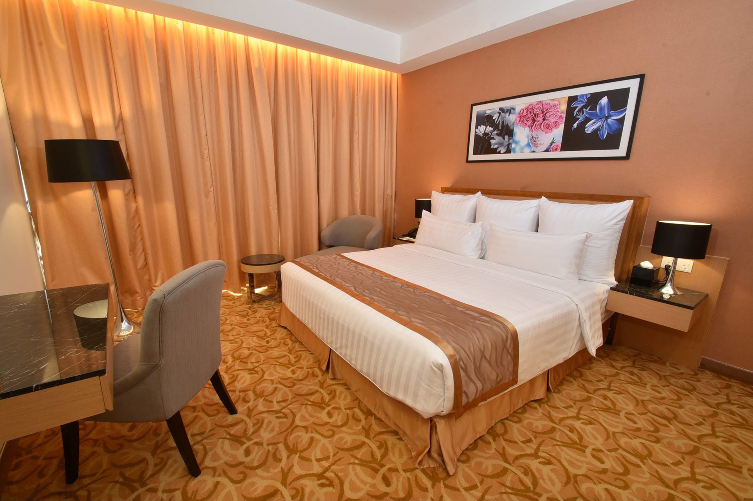 Una habitación de hotel con una cama grande, un escritorio, una silla, una mesita de noche y una lámpara de pared.